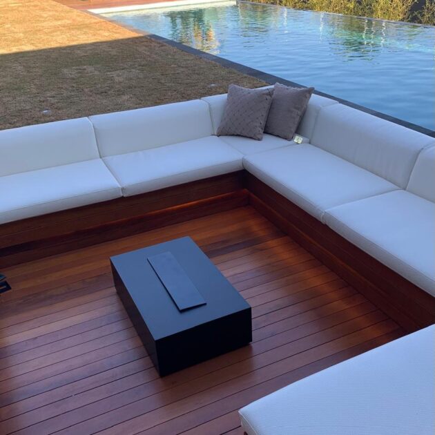 Lounge com sofá sobre deck de madeira ao lado da piscina